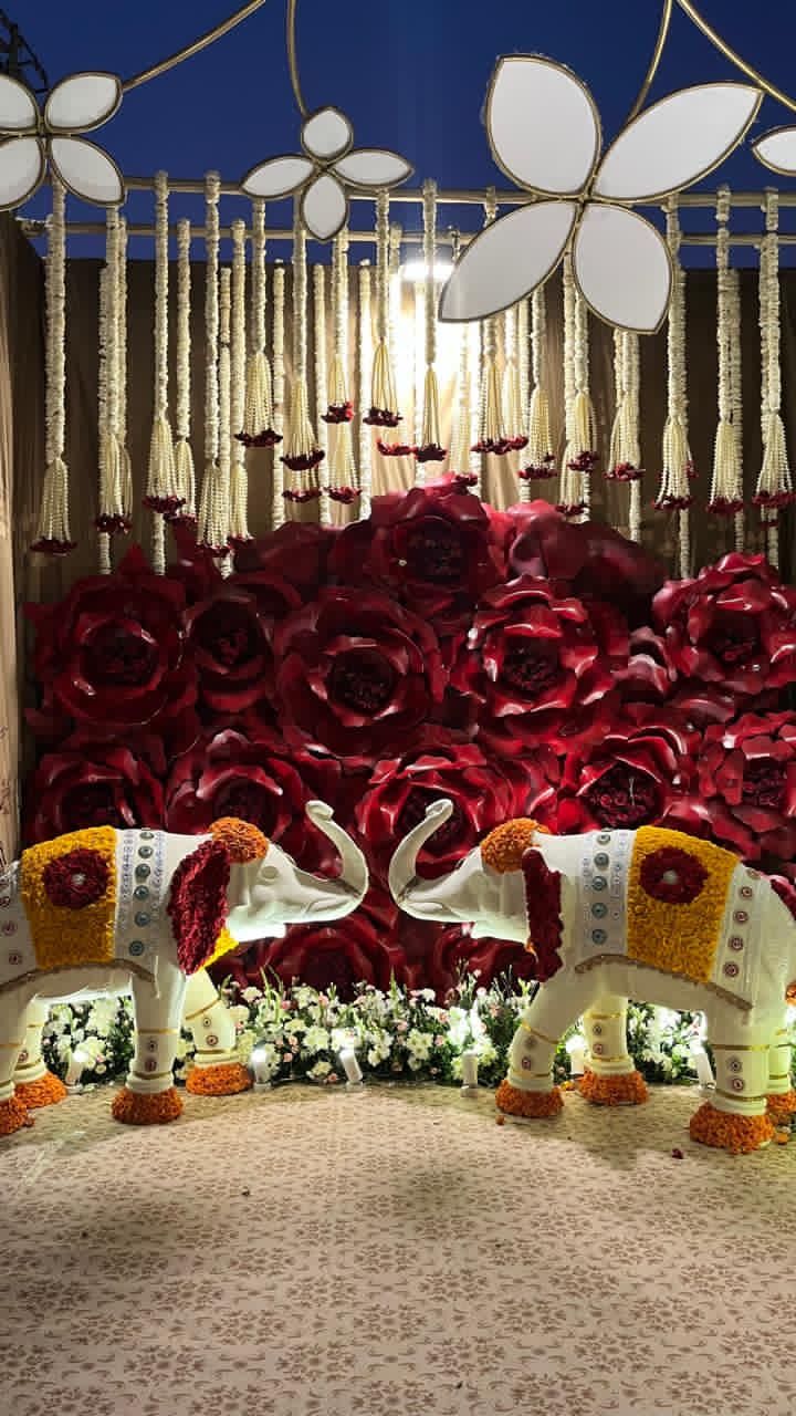 Decorated white elephants before a wall of giant red roses