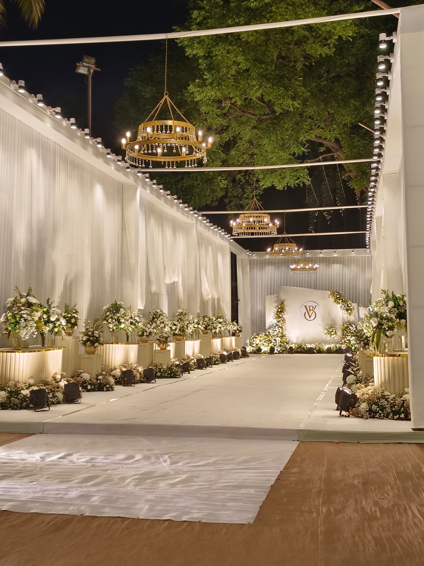 White draped aisle with gold chandeliers and white florals at night